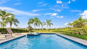 A swimming pool with lounge chairs, surrounded by palm trees and well-maintained hedges. - 7703 Banyon Way (Kissimmee)