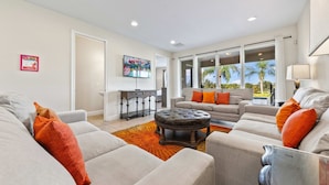 A spacious living room with a large window, a sofa set, and a coffee table. - 7703 Banyon Way (Kissimmee)