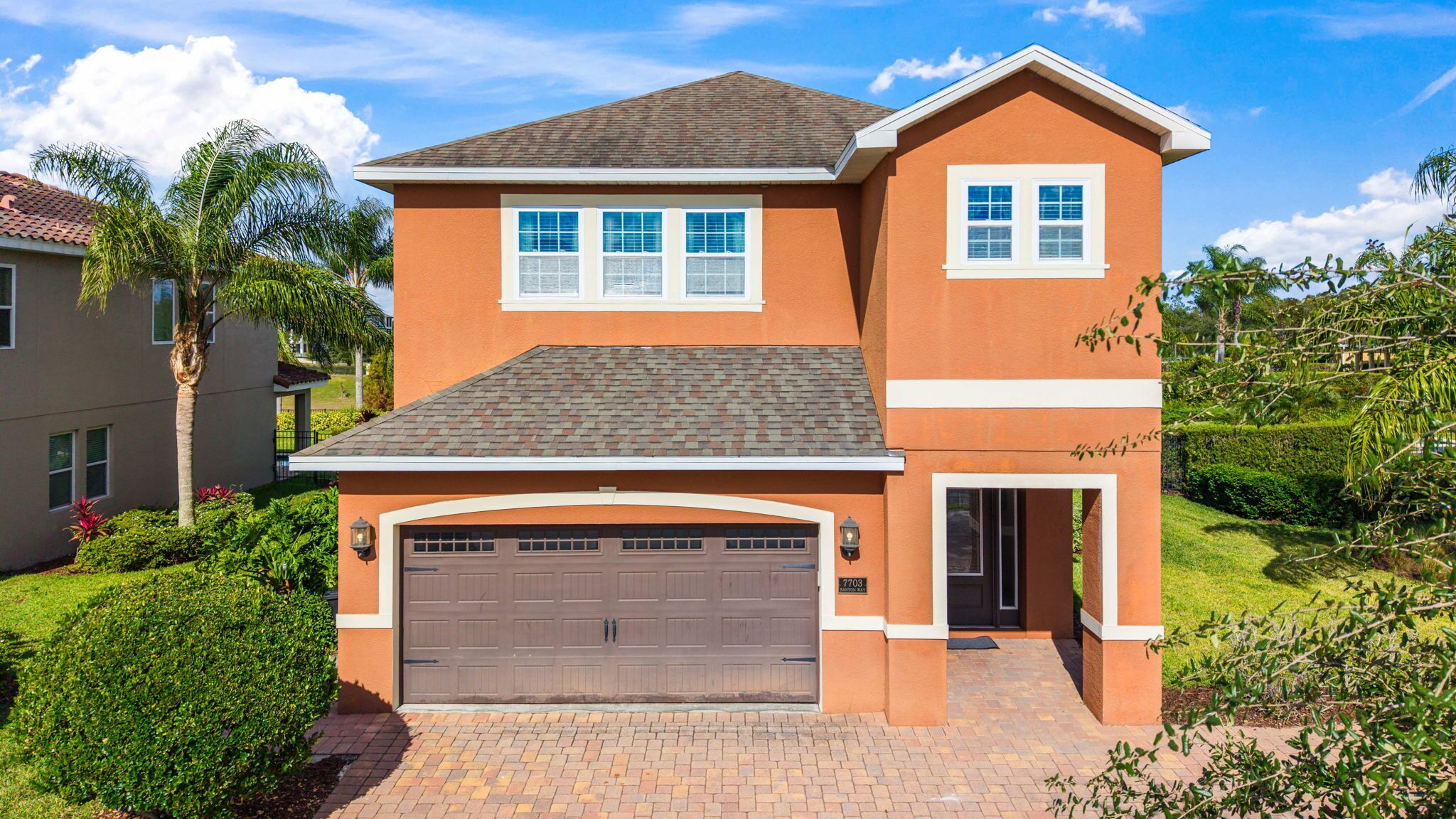 A two-story house with a brown garage door, a small porch, and a well-maintained lawn.