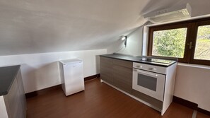 A compact kitchen with a refrigerator, oven, and a window with a view of greenery.