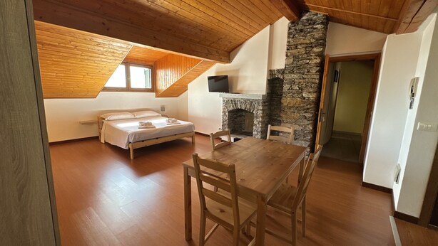 Un dormitorio con cama, una mesa de madera, sillas, una chimenea de piedra y un televisor.