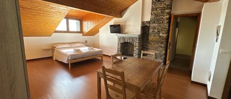 Un dormitorio con cama, una mesa de madera, sillas, una chimenea de piedra y un televisor.