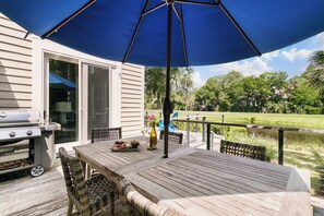 Eine Terrass mit Holztisch, Stühlen, einem Grill und einem großen Sonnenschirm.