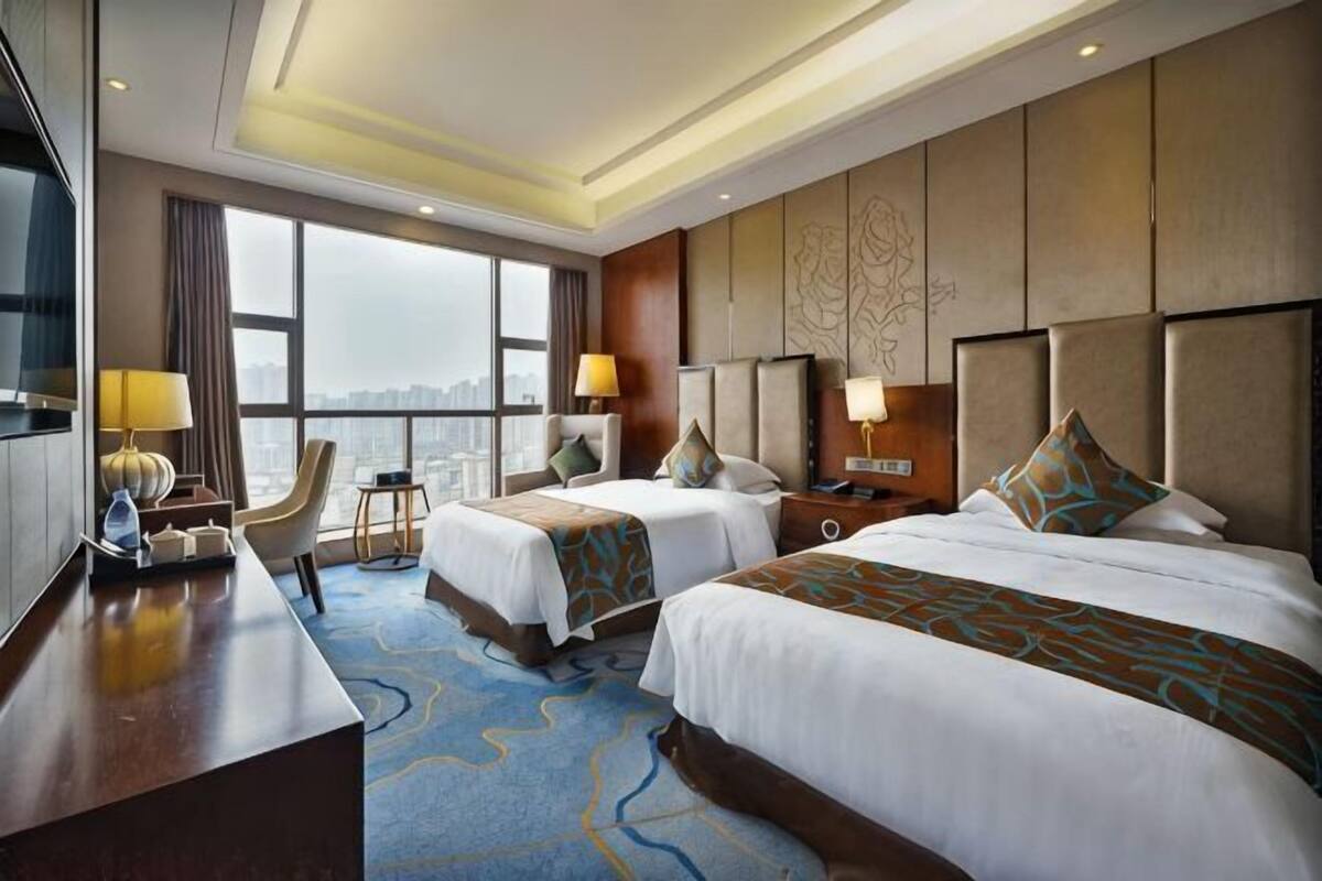 A hotel room with two beds, a desk, a chair, a TV, and a city view.