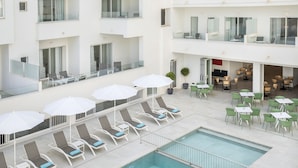 Un hotel con piscina en la azotea, sillones de descanso y mesas para comer al aire libre.