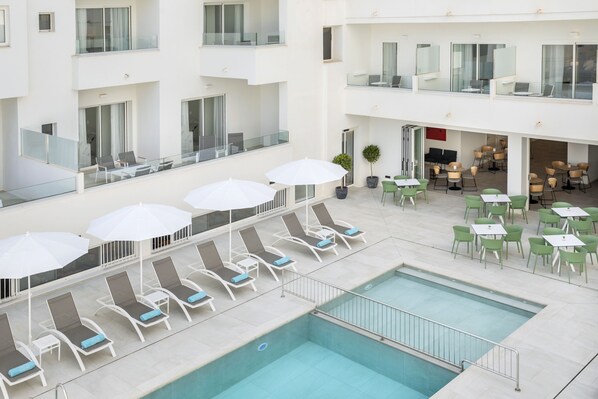 Un hotel con piscina en la azotea, sillones de descanso y mesas para comer al aire libre.