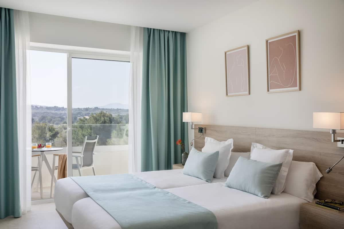 Habitación de hotel con una cama grande, dos lámparas de noche, vistas al exterior y una pequeña mesa con sillas.