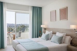 A hotel room with a large bed, two wall-mounted lamps, a nightstand, a chair, a table with a vase, and a view of the outdoors.