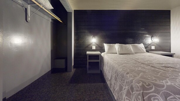 A bedroom with a bed, two bedside tables, and a wall-mounted light fixture.