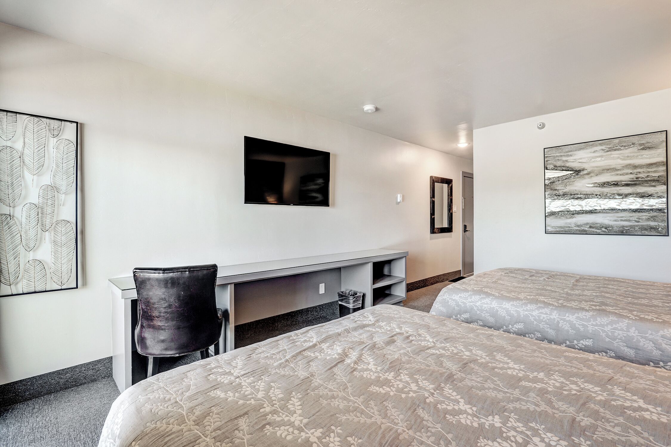 Une chambre d’hôtel avec deux lits, un bureau et une chaise. Les murs sont ornés d’œuvres d’art et le plafond est éclairé par un luminaire.