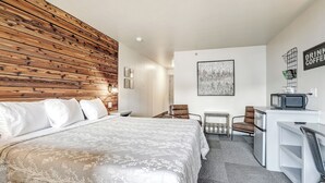 Une chambre d’hôtel avec une tête de lit en bois, un lit avec du linge de maison blanc, un bureau avec une télévision et une chaise.