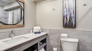 Une salle de bain moderne avec un lavabo blanc, un miroir avec un cadre en bois, des toilettes et un grand tableau abstrait accroché au mur.