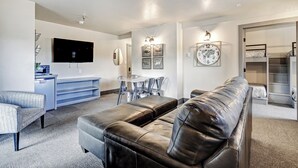 A modern living room with a leather sofa, a dining table with chairs, a flat-screen TV mounted on the wall, and a built-in shelving unit. - In-Town | 2 Bedroom Suite | Elk Horn Lodge 300 (Angel Fire)