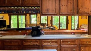 Una cocina con gabinetes de madera, una cafetera y un ventanal con vistas a la vegetación.