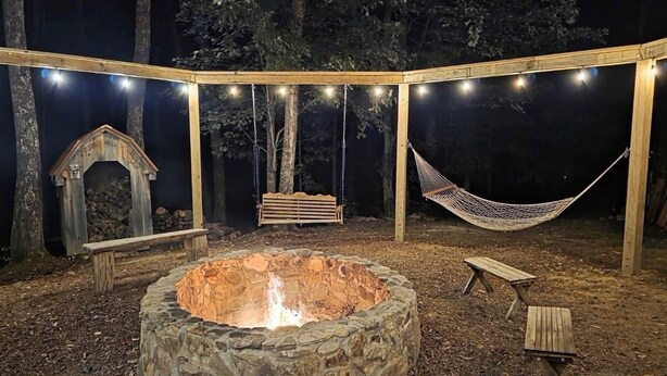 Un espacio al aire libre cubierto con un hogar de piedra, una hamaca y un banco de madera.