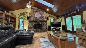 Una sala de estar con chimenea de piedra, sofá de cuero, televisor y una mesa de centro de vidrio.