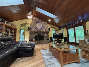 A cozy living room with a stone fireplace, leather sofa, and a flat-screen TV.
