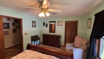 Un dormitorio con cama, cómoda, silla, ventilador de techo y ventana.