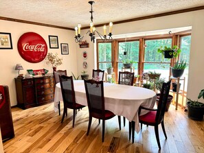 A dining area with a round table, chairs, a chandelier, and a large Coca-Cola sign.