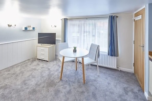 A small, modern room with a round table, a chair, a TV, a radiator, and a window with curtains.
