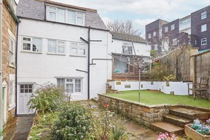 A residential property with a white exterior, a small garden with a lawn and stone steps, and a metal drying rack.