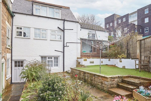 A residential property with a white exterior, a visible garden with a lawn and stone steps, and a brick wall.