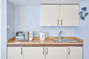 A kitchen with a microwave, kettle, and sink.