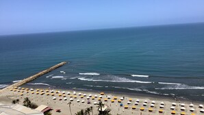 A beach with rows of umbrellas and beach chairs, a rocky breakwater, and the ocean.