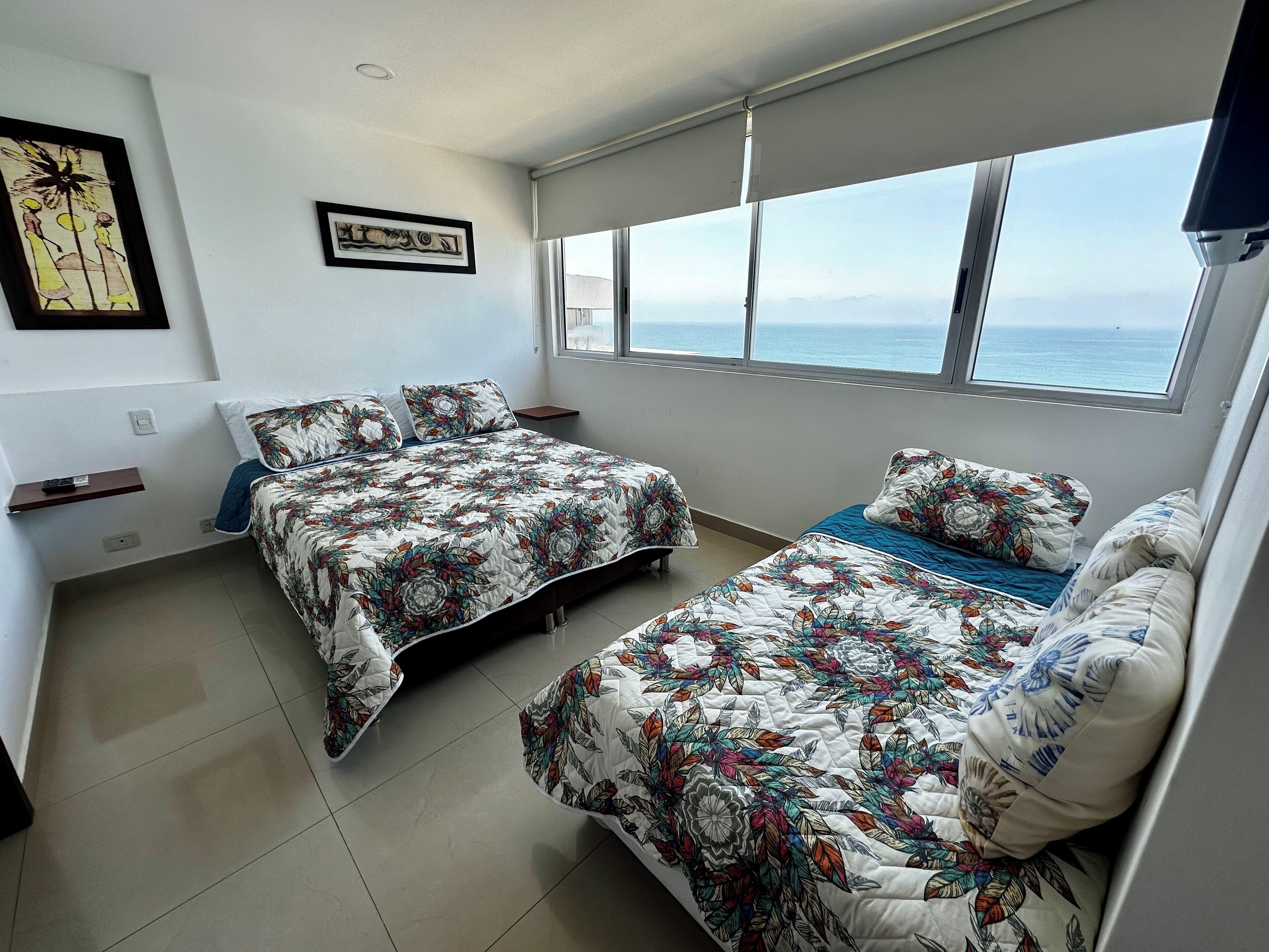 Een slaapkamer met twee bedden, een groot raam met uitzicht op zee en kunst aan de muur.