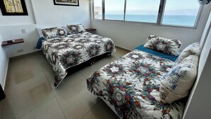 A bedroom with two beds, a large window with a view of the sea, and artwork on the wall.