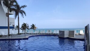 A swimming pool with lounge chairs and palm trees, overlooking the ocean.
