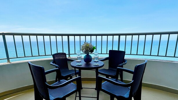 A balcony with a table and chairs, a vase with flowers, and a view of the ocean.