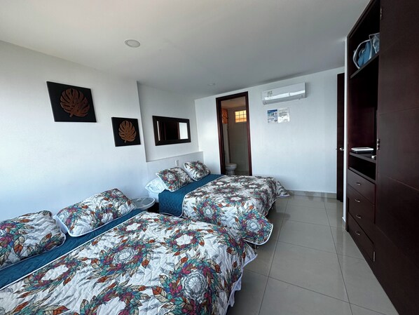Une chambre avec deux lits, une armoire et une salle de bain visible à travers une porte ouverte.