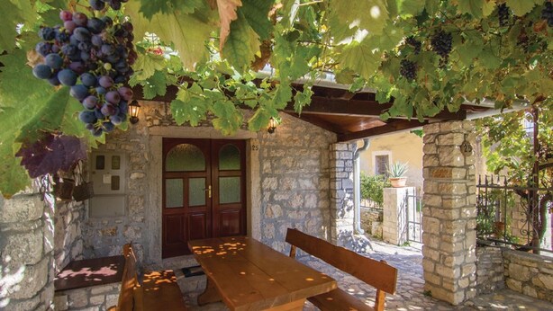 An outdoor seating area with stone walls, a wooden table, and benches. - Holiday House Marina (Sveti Lovrec)