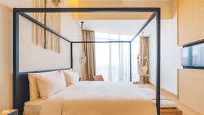 Une chambre d’hôtel moderne avec un lit à baldaquin, une table de chevet en bois, une petite table et une grande fenêtre avec des rideaux.