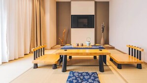 Une pièce de style japonais traditionnel, avec un sol recouvert de tatamis, une petite table basse entourée de coussins et un téléviseur fixé au mur.