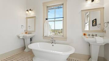 Une salle de bain avec une baignoire sur pieds, deux lavabos et une grande fenêtre.