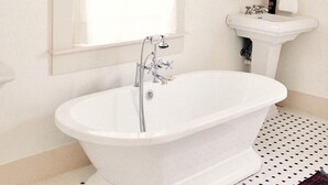 A bathroom with a freestanding bathtub, a pedestal sink, a mirror, and a window with a curtain.