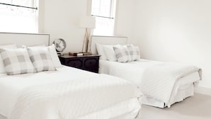 A bedroom with two beds, a nightstand, a lamp, and a window.