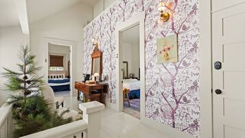 A hallway with a staircase leading to a bedroom. There is a Christmas tree and a mirror on the wall.
