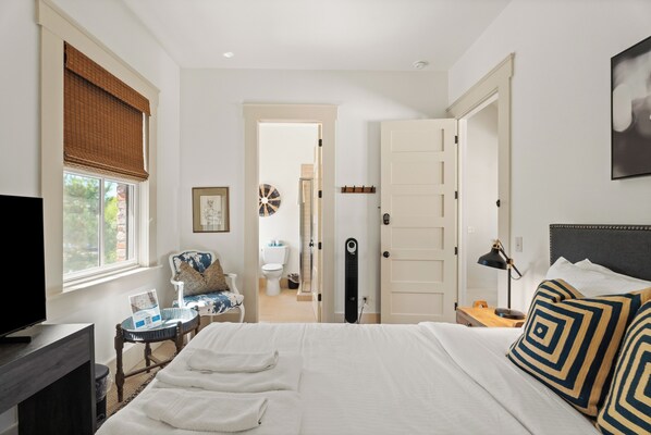 Habitación de hotel con cama, escritorio, silla, televisión y ventana con persianas.