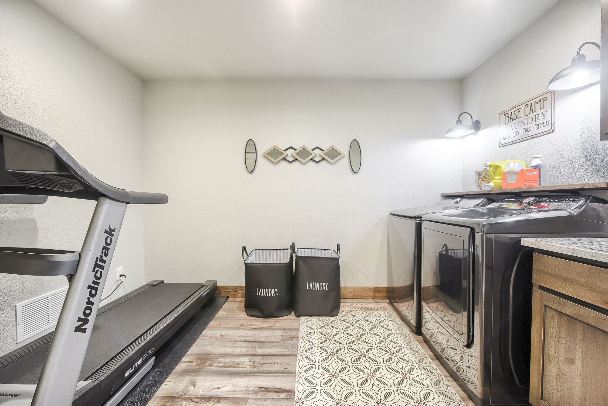 A compact laundry room with a Nordica treadmill, a washing machine, and two laundry bags labeled "laundry."
