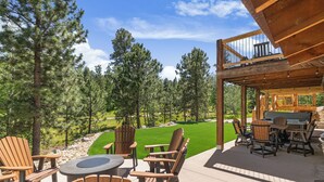 An outdoor patio with Adirondack chairs, a round table, and a grill area. - Stunning 3700+ Sq. Ft Lodge w/ Firepit, Hot Tub, Large Garage - Paved! (Lead)