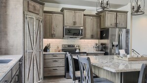 A modern kitchen with wooden cabinets, a built-in microwave, an oven, and a refrigerator. There are two bar stools and a granite countertop. - Stunning 3700+ Sq. Ft Lodge w/ Firepit, Hot Tub, Large Garage - Paved! (Lead)