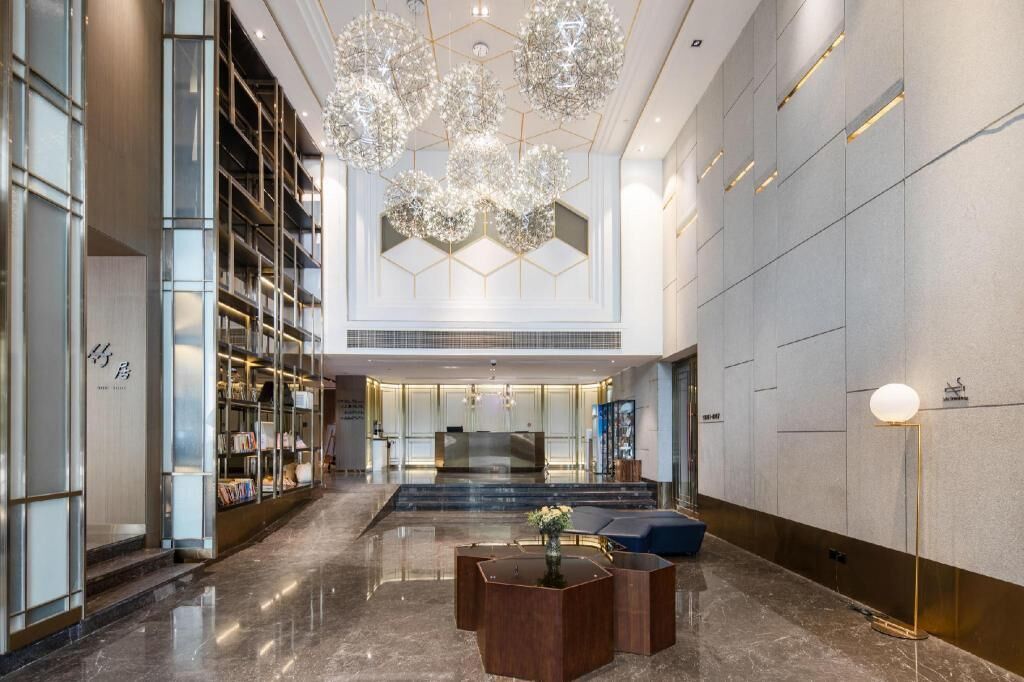 Un moderno vestíbulo de hotel con una recepción, un área de descanso y una amplia estantería.