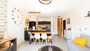 A modern kitchen with a dining area, a sofa with a yellow pillow, and a coffee table with a candle. - Appartment Christine in Lège city for 5 persons (Lège-Cap-Ferret)