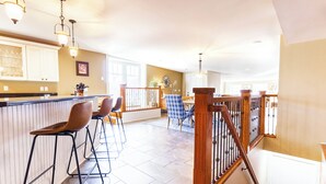 A spacious kitchen with high ceilings, a wooden staircase, and a bar area with stools.