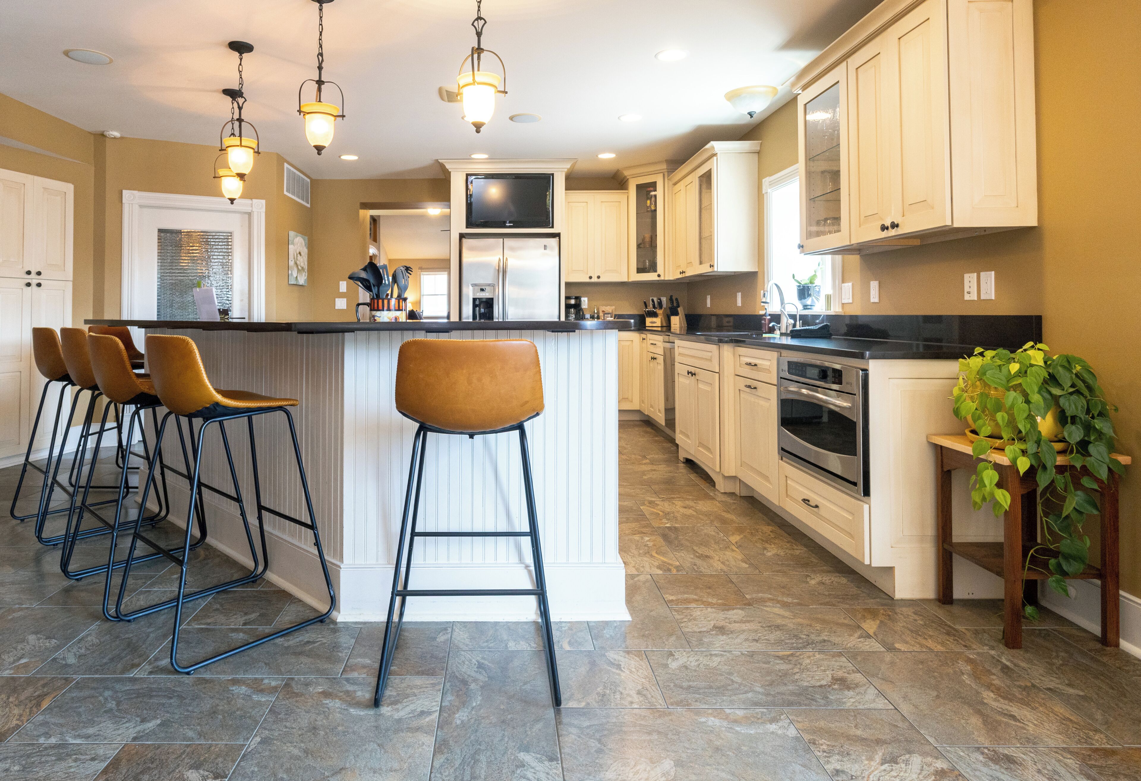 A kitchen with a central island, bar stools, a refrigerator, an oven, and a sink.