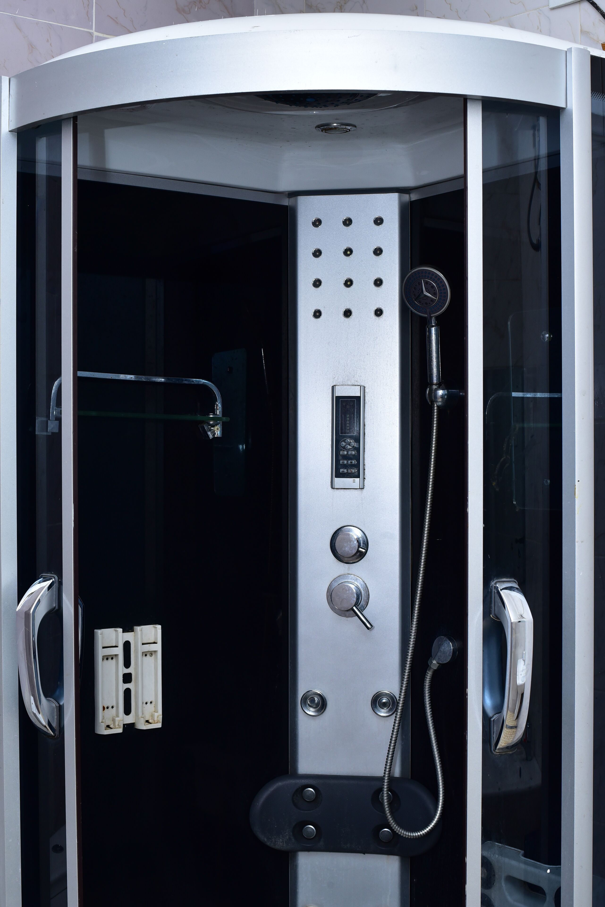 A modern, enclosed shower stall with a control panel, a handheld showerhead, and a glass door.