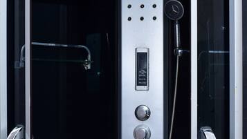 A modern, enclosed shower stall with a control panel, a handheld showerhead, and a glass door.